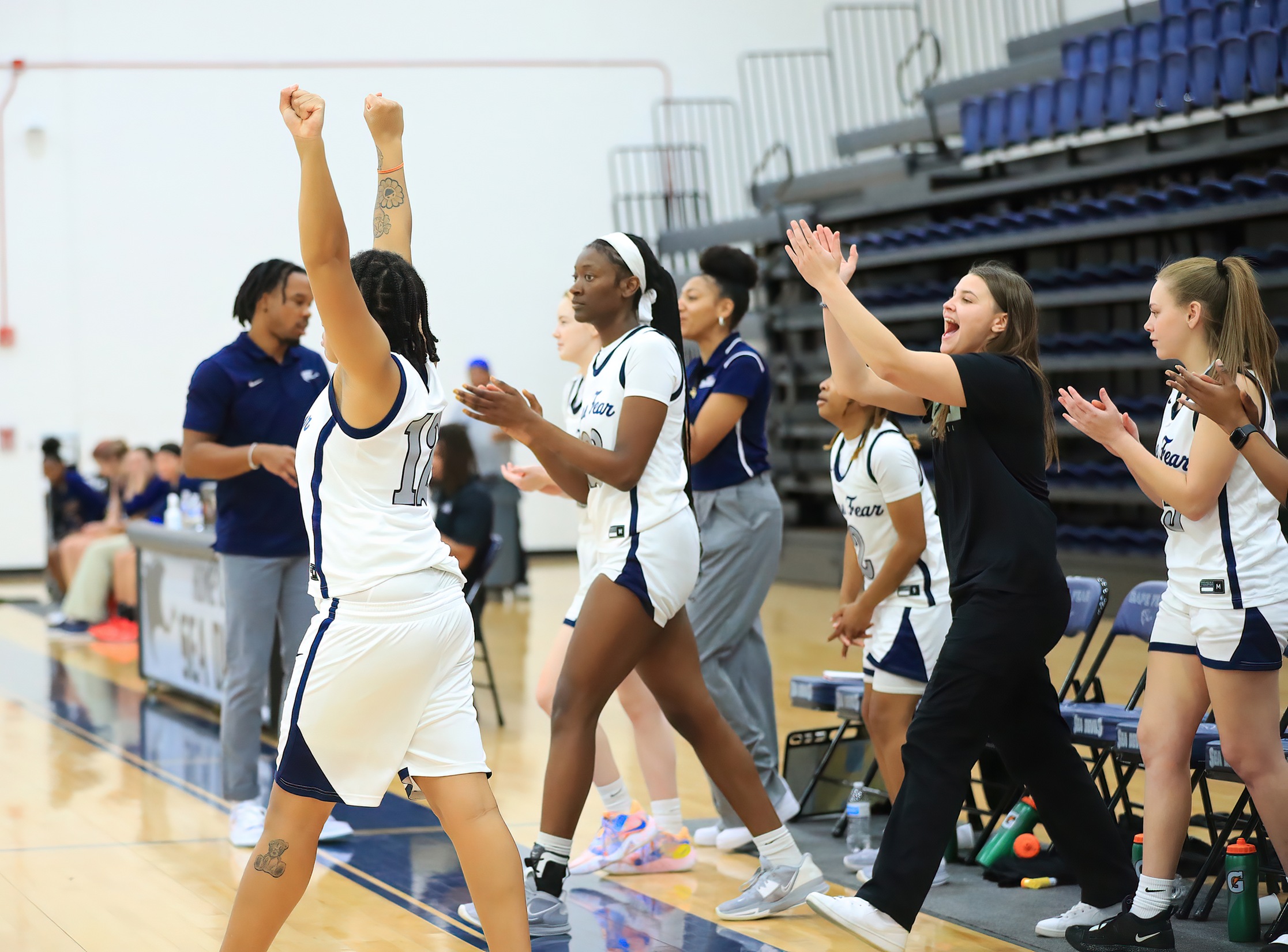Multiple CFCC Women's Basketball players cheering and coming onto the court to celebrate a good play