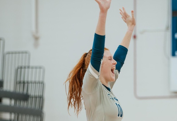 CFCC volleyball player celebrating earned point with hands in the air.