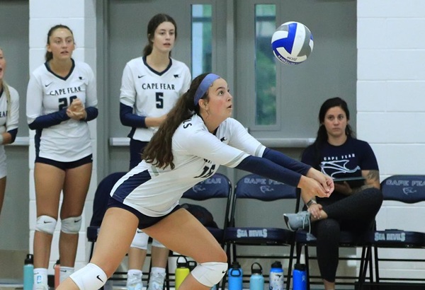 action shot of Isa Yedo bumping a volleyball with some teammates on the sideline pictured behind her