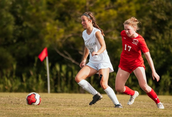 CFCC women's soccer player dribbling a ball down the field followed by a Louisburg player defending.